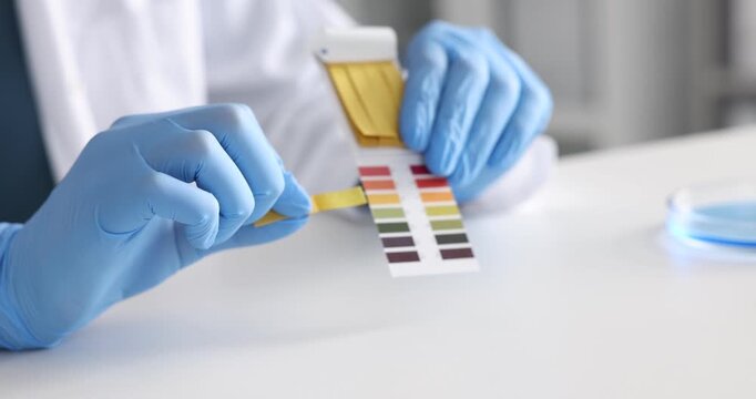 Scientist holding PH test strips with color table at white table in laboratory, closeup