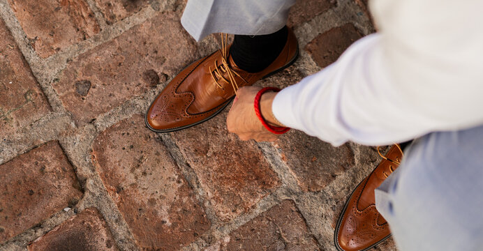 Hombre ajustando los cordones de zapatos de cuero marr&oacute;n con traje elegante sobre pavimento de piedra