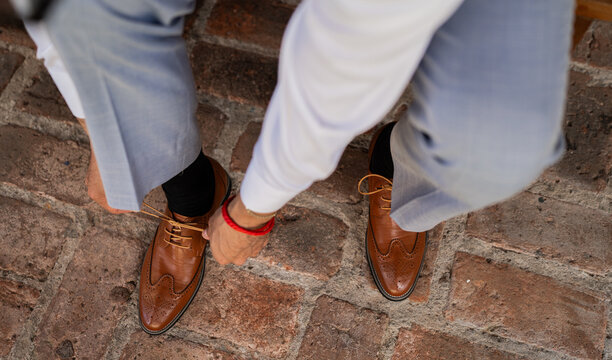 Hombre elegante ajustando los cordones de zapatos de cuero marr&oacute;n con traje formal sobre piso adoquinado