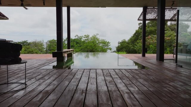 Stunning villa in Costa Rica features an infinity pool surrounded by wooden deck and lush tropical vegetation. Modern architecture blends with natural rainforest landscape under cloudy skies.