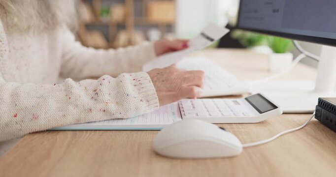 Senior woman uses calculator for bills payment. At a home office desk she tracks monthly expenses and balances a tight household budget using a computer. Clear concept of budgeting and payment.