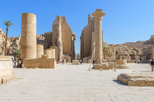 Tourists sightsee at the First Courtyard (or Forecourt) of the Karnak Temple Complex, located in Luxor, Egypt, with the Column of Taharqa and Colossal Statue of Ramesses II in view.
