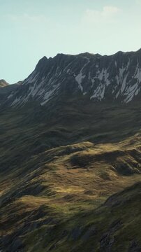 Mountain landscape shows slopes with green grass and some rocky areas. Light shines on the terrain, displaying the natural shapes of the land. This scene captures morning light on hills.