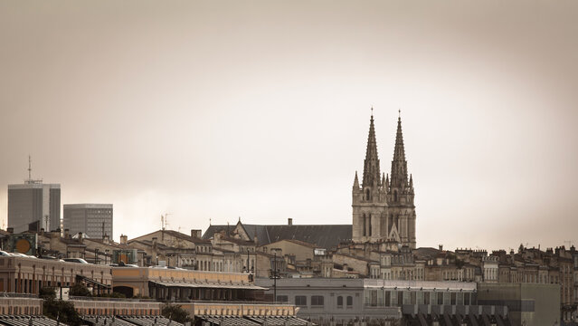 View from the Garonne quay at Les Hangars Village Bord'eau in Bordeaux, France, with Saint Andre Cathedral rising behind riverside buildings and the urban skyline in soft light in southwestern France.