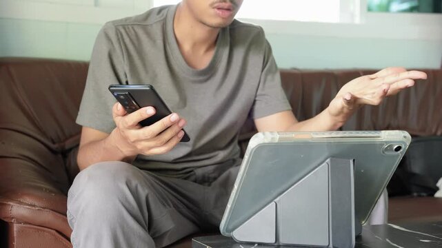 Young businessman greeting colleagues via digital tablet while remote work at workplace. Conversations, meetings, business teams, and working from home. Person use technology AI chat bot or online