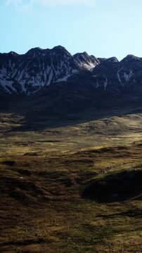 Mountains rise in the background with green hills in the foreground. The sun shines brightly over the scene creating light and shadows on the ground during daytime.