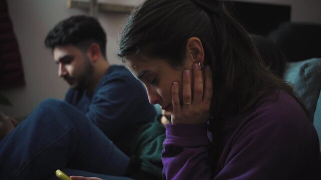 Group of young Hispanic friends sitting on a sofa, each focused on their own smartphone without interacting, illustrating digital distraction, social disconnection, and modern technology habits at hom
