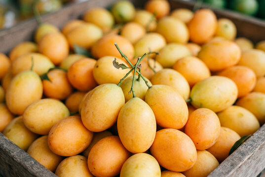 A vibrant full frame arrangement of numerous ripe yellow maprang fruits in a rustic wooden crate