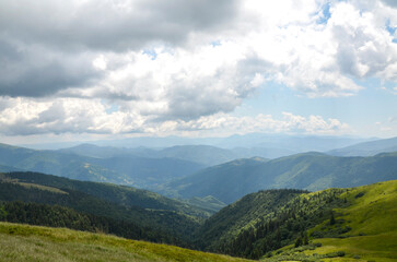 Fototapeta premium Dramatic sunlight and cloud shadows sweep across lush green ridges and vast, rolling mountain ranges stretching toward the horizon under a heavy, overcast sky. Carpathian Mountains, Ukraine 