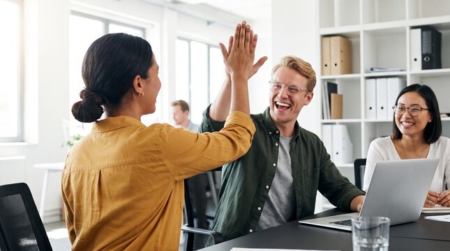 Enthusiastic business colleagues high-fiving in a modern office, celebrating a successful project and strong teamwork in a collaborative environment