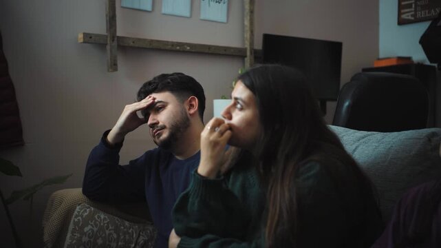 Three young Hispanic friends sitting on a sofa feeling bored and uninterested while watching a movie on TV, expressing lack of engagement during a quiet evening at home.
