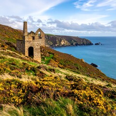 Fototapeta premium A weathered stone structure stands on a grassy hillside, overlooking a vibrant ocean with distant cliffs under a cloudy sky