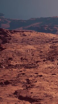 A rocky terrain stretches across the surface of a distant planet. The ground displays red soil and scattered stones, while a dark sky looms in the background, hinting at a vast landscape.