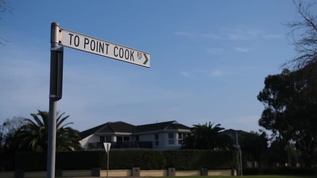 A directional street sign reading "TO POINT COOK RD" at a suburban roadside. Traffic and contemporary double-story family home in background. Melbourne Australia