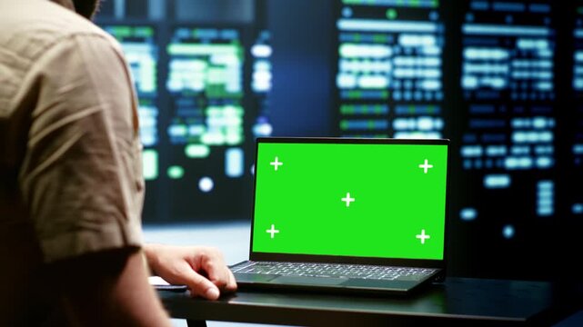 Computer scientist checks mainframes with a laptop mockup in a data center, keeping the green screen display ready for screen replacement and post production during green screen laptop.