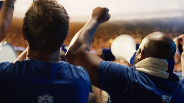 Close up of football supporters waving scarves and chanting with megaphone in stadium, showing soccer fans wearing blue team colors in sports arena showing energetic support with props.