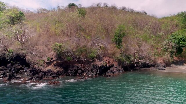 Low-altitude drone footage capturing volcanic rock formations, rugged coastal cliffs, and turquoise Caribbean waters in Saint Vincent and the Grenadines. Detail shot of the natural shoreline and folia