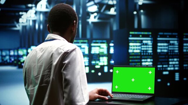African American engineer checks server cabinets with a laptop mockup in a data center during chroma key laptop server.