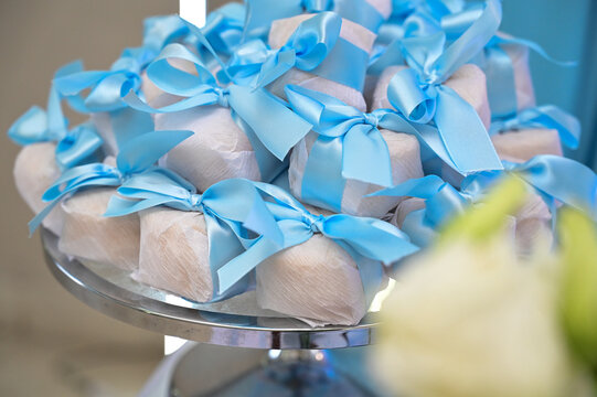 traditional bem casado wedding sweets with blue ribbon, wrapped party favors on elegant glass stand, baby shower sweet souvenir gift presentation, brazilian confection close up