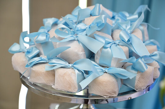 traditional bem casado wedding sweets with blue ribbon, wrapped party favors on elegant glass stand, baby shower sweet souvenir gift presentation, brazilian confection close up