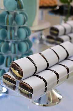 wrapped chocolate brownies on elegant acrylic stand, gourmet party favours at luxury wedding dessert buffet, sweet confectionery presentation with blurred macarons tower background