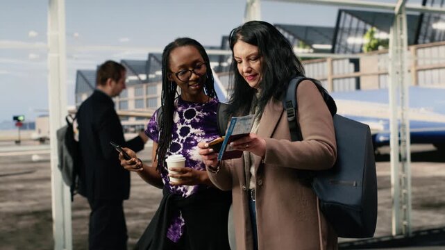 Cheerful friends in airport watching videos on smartphone, having fun, happy female tourists in airport terminal using a mobile phone to look at social media.