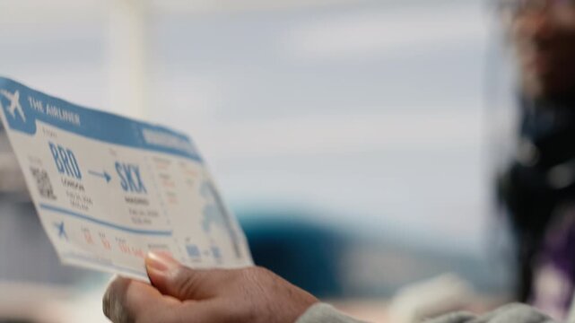 Close up of airplane ticket used by people walking in airport terminal traveling together to foreign countries, African American man and woman reading boarding pass flight information.