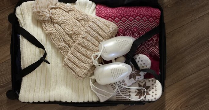 Hand puts boot dryer in suitcase with winter clothes for travel. Top view	
