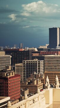 People look at a city skyline filled with tall buildings and various structures under a cloudy sky. The view shows a mix of architecture with a hint of distance.