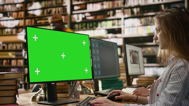 Green screen mockup on desktop near student at shared library table with peers, computer class with people using monitors, for education technology.