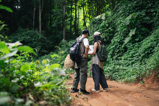 Young couple hiking together on a forest trail surrounded by dense green foliage and tall trees during outdoor adventure walk