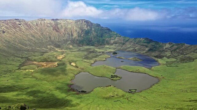 Wide aerial view of lush volcanic crater with lakes and ocean in the background, daytime