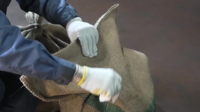 Worker kneels beside a burlap sack securing a bundle of chains with wire and pliers