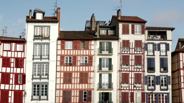 Row of classic Basque half timbered buildings with red and blue window shutters under a clear sky in Bayonne.