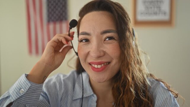 Woman with headset holding microphone and smiling, american flag visible on wall in campaign building; voter outreach pride.