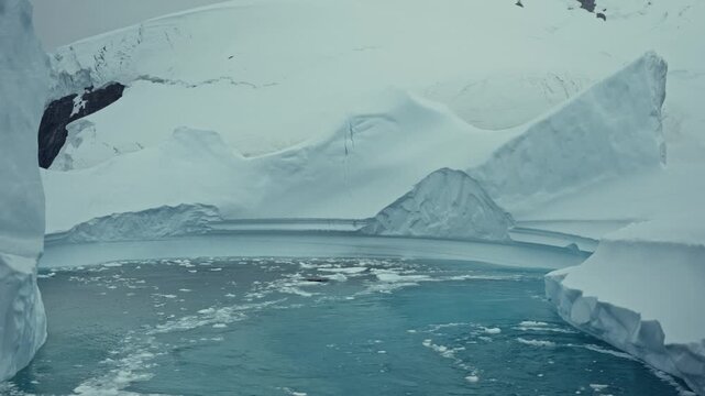 View through narrow glacier channel reveals iceberg dotted water under overcast sky