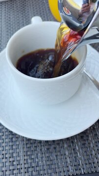 UGC style vertical video pouring coffee into white mug in hotel or cafe. Morning breakfast at resort buffet or restaurant. Serving black filtered coffee into cup. Point of view shot. Travel vlogger