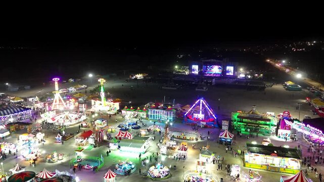 Drone continues pushing over the Mexican fair in San Jose del Cabo, moving past carnival rides and flashing lights toward the concert venue and crowd gathered behind the fairground.
