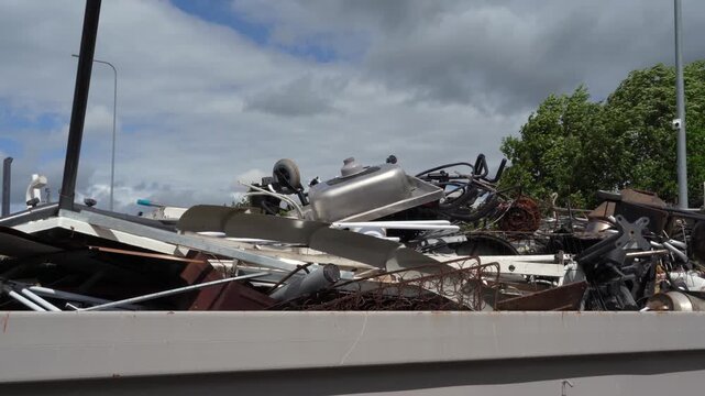 Rusting scrap metal and old appliances fill a high-sided skip under cloudy skies during a recycling trip.