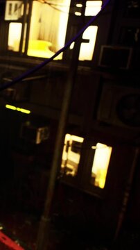 Workers are in a city building at night. Lights are on in several windows. The scene shows parts of the building and equipment outside. It looks busy and active during evening hours.
