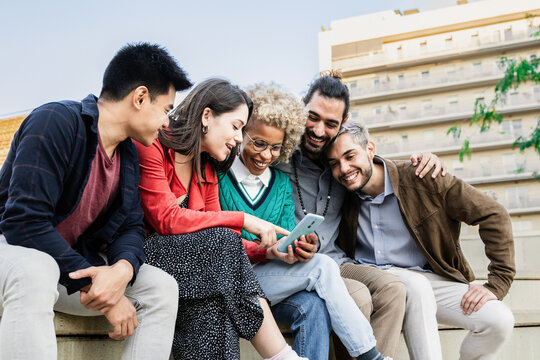 Young multiracial group of friends using mobile smartphone sitting on urban stairs - Youth lifestyle and technology concept