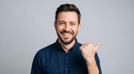 Fototapeta premium Smiling man with beard pointing thumb to the side on grey background