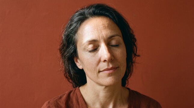 Woman with eyes closed in meditation or deep thought against a warm terracotta background