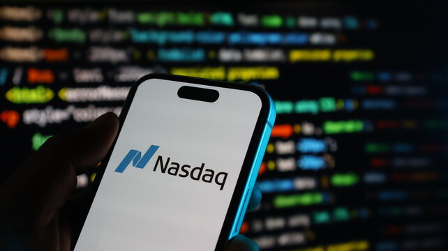 Hand holding smartphone with nasdaq logo on screen with blurry colorful stock market data in background
