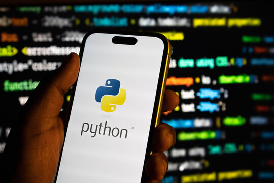 Closeup of a hand holding a smartphone displaying the python programming language logo against a background of code