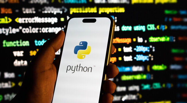 Hand holding a smartphone displaying the python programming language logo against a background of computer code