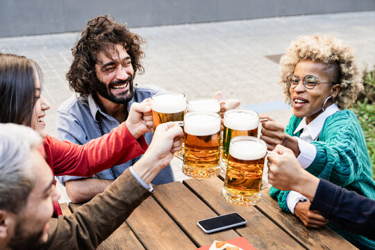 Group of diverse friends have fun in dinner party outdoors - Young people toasting at bar table with beer glasses