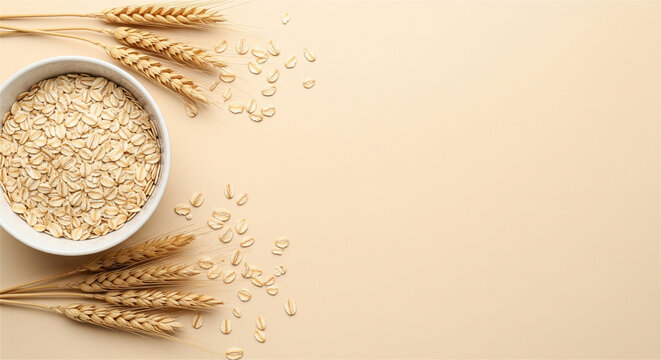 Raw oatmeal in white bowl with wheat ears, healthy breakfast ingredients on beige background, organic oat flakes flat lay with copy space