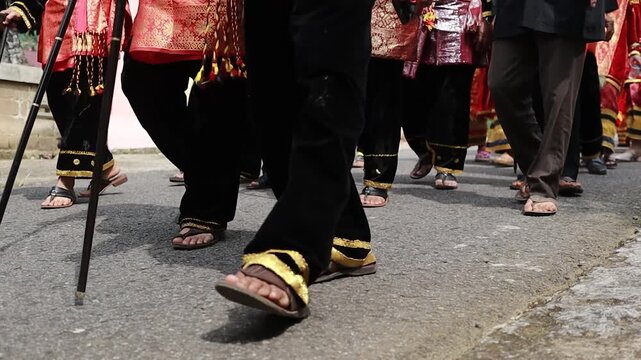 Close-up shot of feet walking in traditional Minangkabau attire, wearing cultural pants, a sarong skirt, and traditional sandals, reflecting the authentic everyday fashion and cultural identity of the