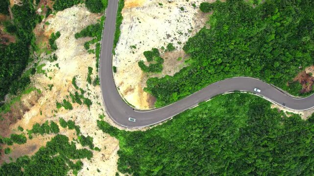 Cars on a winding road through green mountains from above